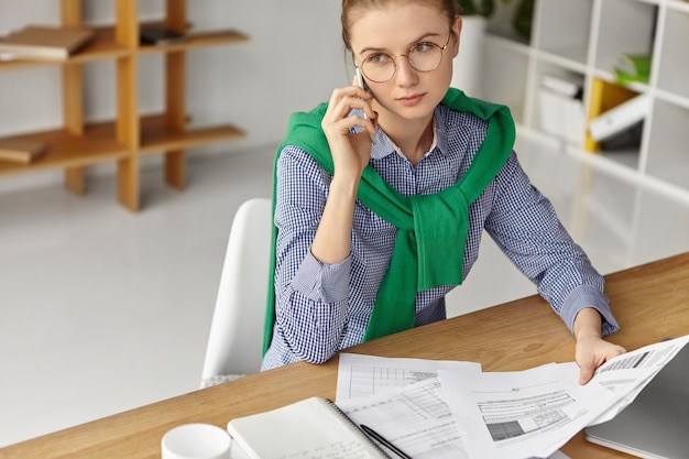 Schöne Frau, die formell im Büro mit Telefon gekleidet ist