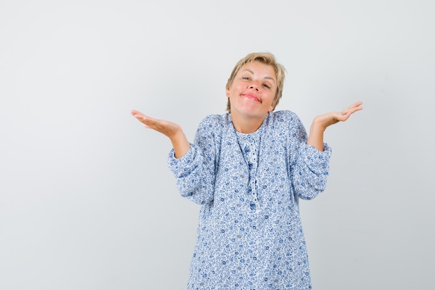 Schöne Frau, die idk Geste in gemusterter Bluse zeigt und faul schaut. Vorderansicht.