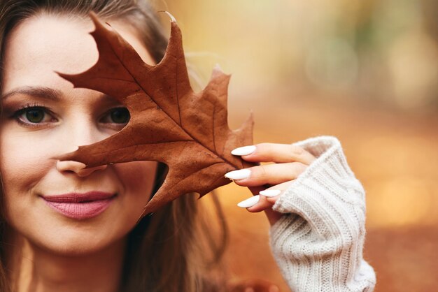 Schöne Frau, die ihr Gesicht mit Herbstblättern bedeckt