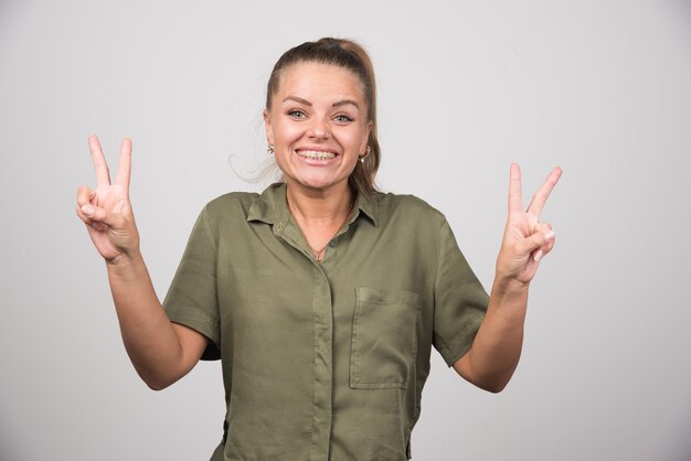 Schöne Frau, die ihre Finger auf grauer Wand zeigt.