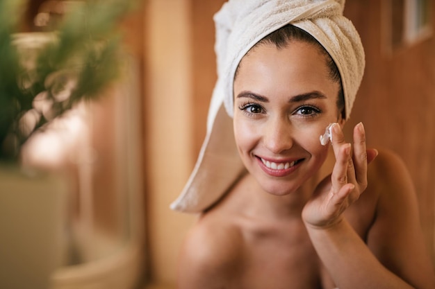 Schöne Frau, die im Badezimmer Feuchtigkeitscreme auf ihr Gesicht aufträgt