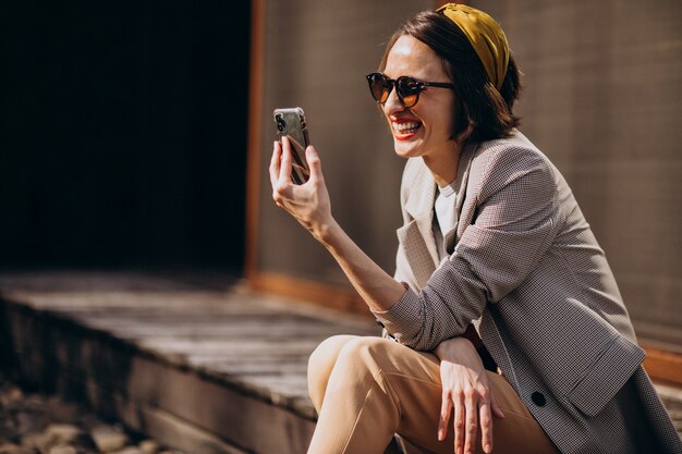 Schöne Frau, die im Hinterhof sitzt und Telefon benutzt