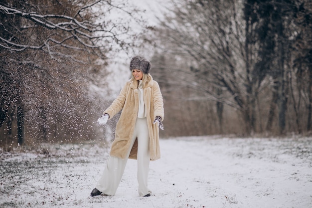 Schöne Frau, die im Park voller Schnee spazieren geht