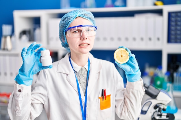 Schöne Frau, die im Wissenschaftlerlabor arbeitet und Pillen und Zitrone in der Hand hält, ahnungsloser und verwirrter Gesichtsausdruck, zweifelt an dem Konzept