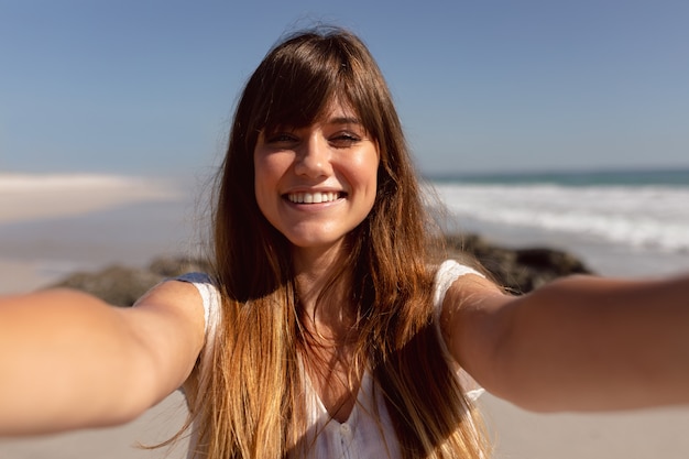 Schöne Frau, die Kamera auf Strand im Sonnenschein betrachtet