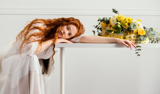 Kostenloses Foto schöne frau, die mit blumenstrauß der frühlingsblumen auf dem tisch aufwirft