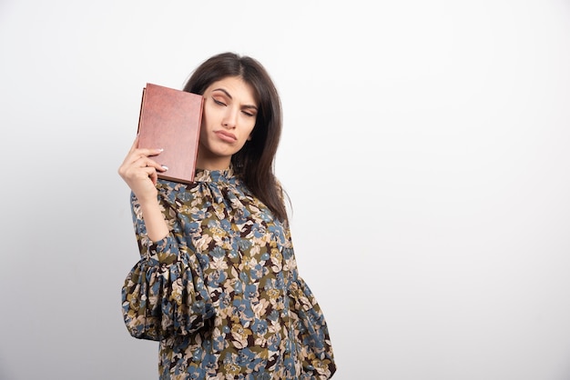 Schöne Frau, die mit Buch auf weißem Hintergrund aufwirft.