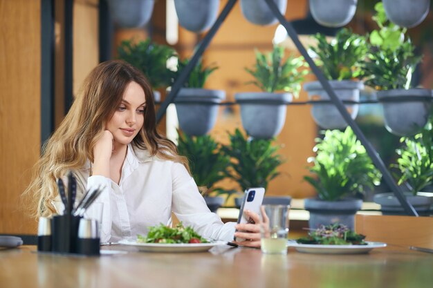 Schöne Frau, die mit Freunden auf modernem Telefon chattet