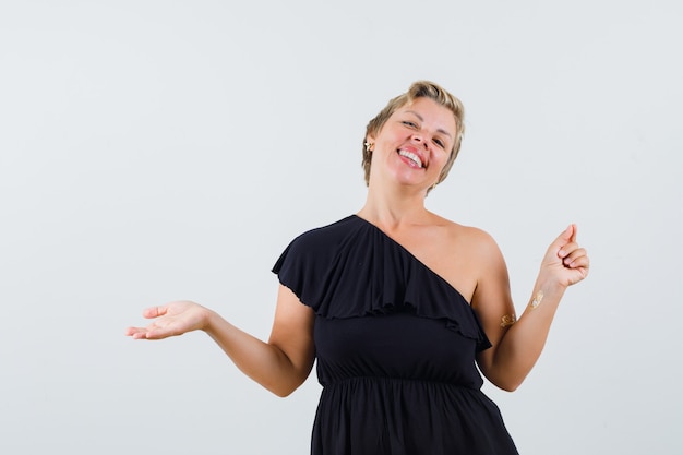 Schöne Frau, die offene Handfläche beiseite spreizend zeigt etwas in der schwarzen Bluse und glücklich aussehend.