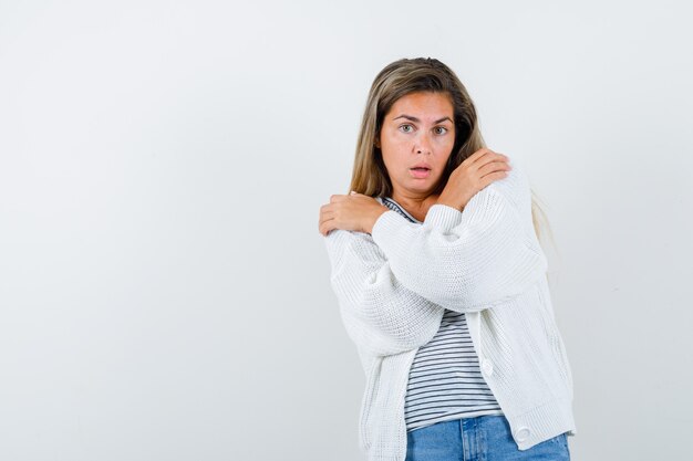 Schöne Frau, die sich in Jacke umarmt und ängstlich aussieht. Vorderansicht.