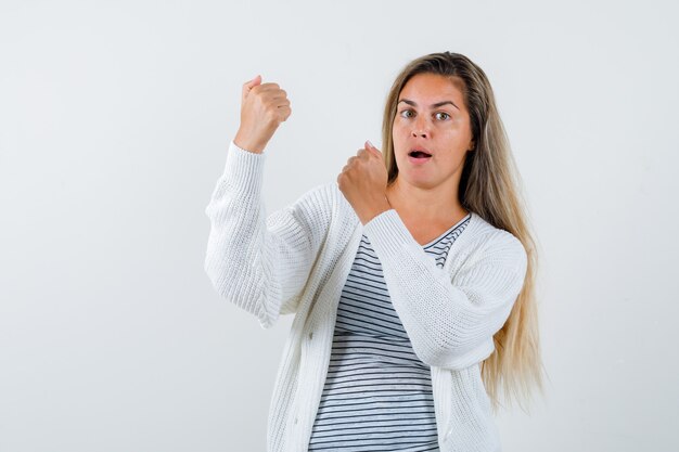 Schöne Frau, die Siegergeste in der Jacke zeigt und überrascht schaut. Vorderansicht.