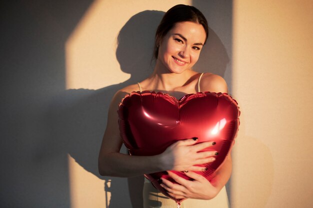 Schöne Frau, die Valentinstag feiert, während sie einen roten herzförmigen Ballon hält