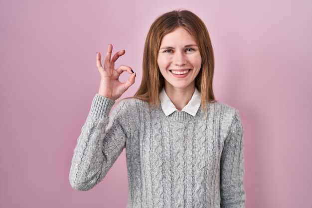 Kostenloses Foto schöne frau, die vor rosafarbenem hintergrund steht und positiv lächelt und mit händen und fingern ein gutes zeichen macht, das einen erfolgreichen ausdruck zeigt