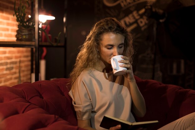 Schöne Frau, die zu Hause ein Buch beim Trinken des Tees liest