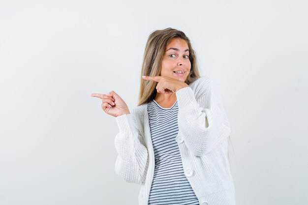 Schöne Frau, die zur Seite in der Jacke zeigt und niedlich, Vorderansicht schaut.