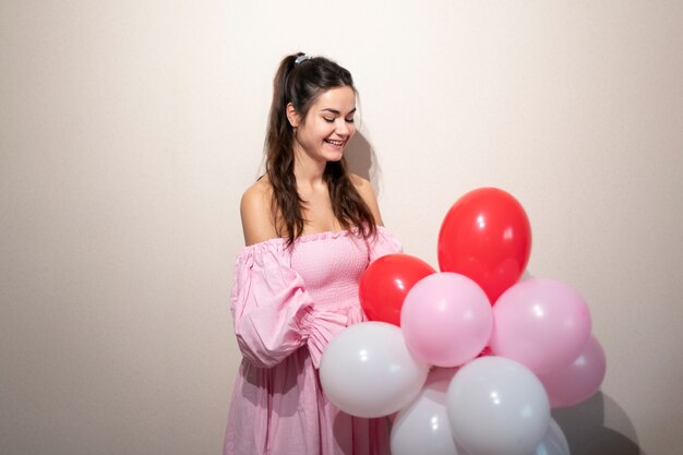 Schöne Frau feiert Valentinstag in einem rosa Kleid mit Luftballons