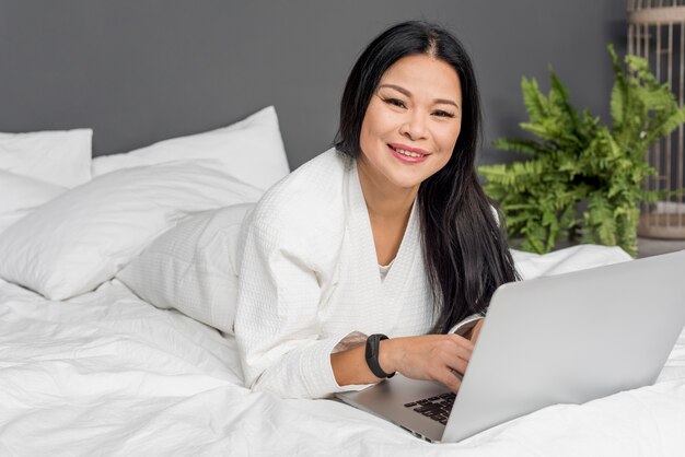 Schöne Frau im Bett mit Laptop gelegt