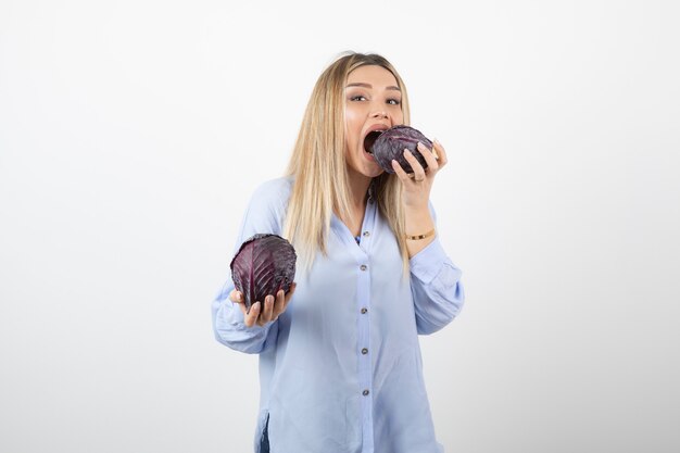 Schöne frau im blauen outfit, die kohl auf weißer wand isst.