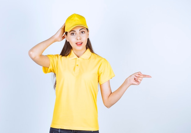 Schöne Frau im gelben T-Shirt und in der Kappe, die irgendwo auf weißem Hintergrund zeigt.