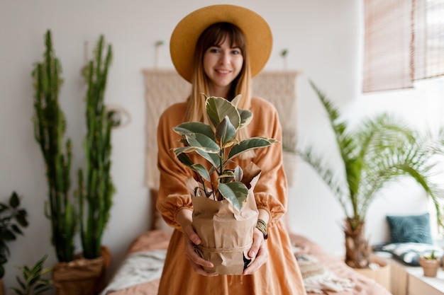 Schöne frau im leinenkleid und im strohhut, die in der wohnung im boho-stil aufwirft