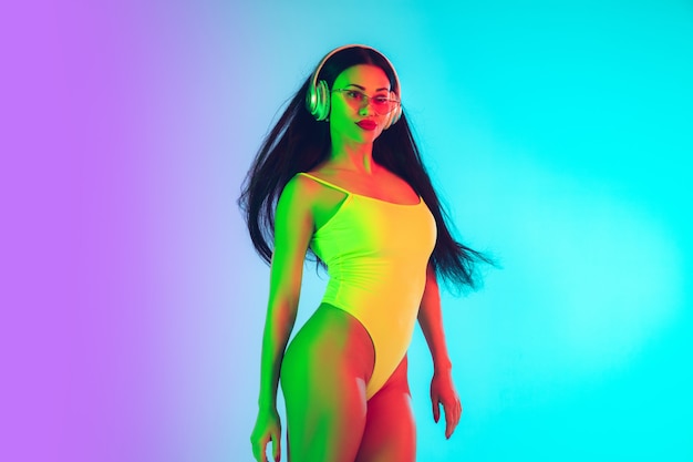 Schöne Frau im modischen Badeanzug isoliert auf einer Studiowand mit Farbverlauf im Neonlicht.