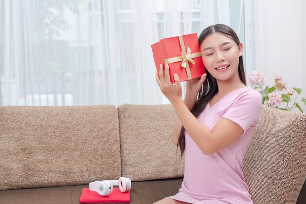 Schöne Frau im rosafarbenen Kleid, sitzend auf dem Sofa und öffnen eine Geschenkbox.