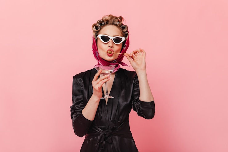 Kostenlose Foto schöne frau im seidenoutfit und in der sonnenbrille, die martini-glas hält und olive isst