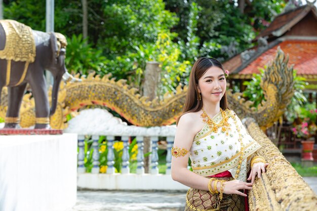 Schöne Frau im thailändischen traditionellen Outfit, das am Tempel lächelt und steht