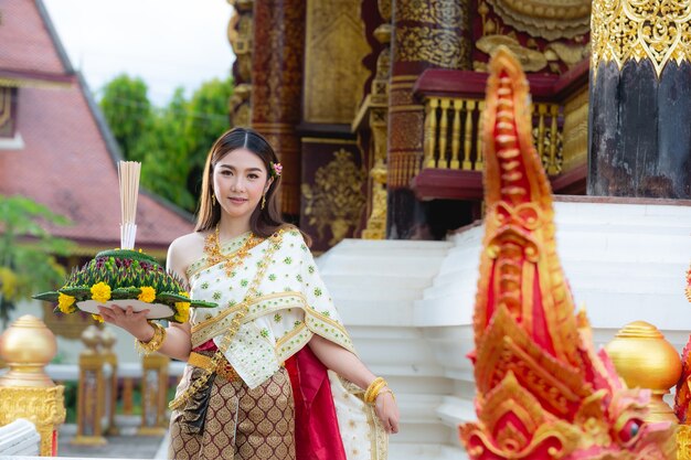 Schöne Frau im thailändischen traditionellen Outfit, das am Tempel lächelt und steht