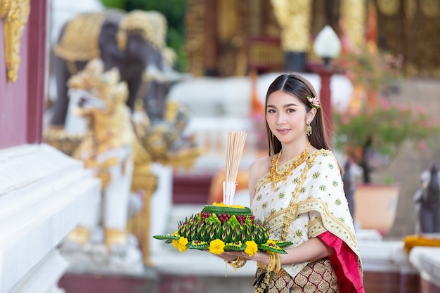 Schöne Frau im thailändischen traditionellen Outfit, das am Tempel lächelt und steht