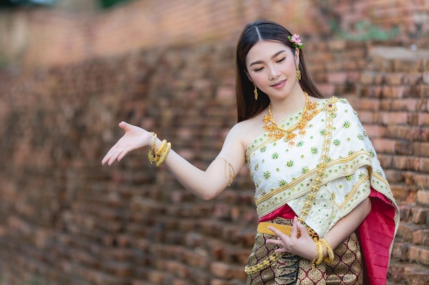 Schöne Frau im thailändischen traditionellen Outfit, das am Tempel lächelt und steht