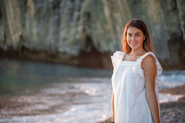 Schöne Frau im weißen Kleid stehend und schauend, in der Küste während des Sonnenuntergangs.