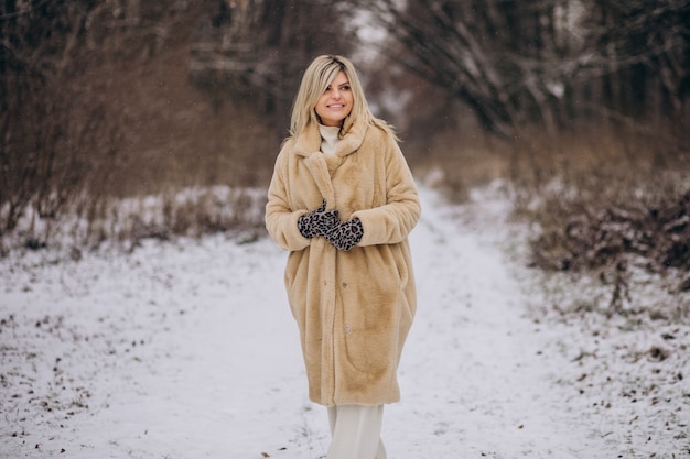 Schöne Frau im Wintermantel zu Fuß im Park voller Schnee