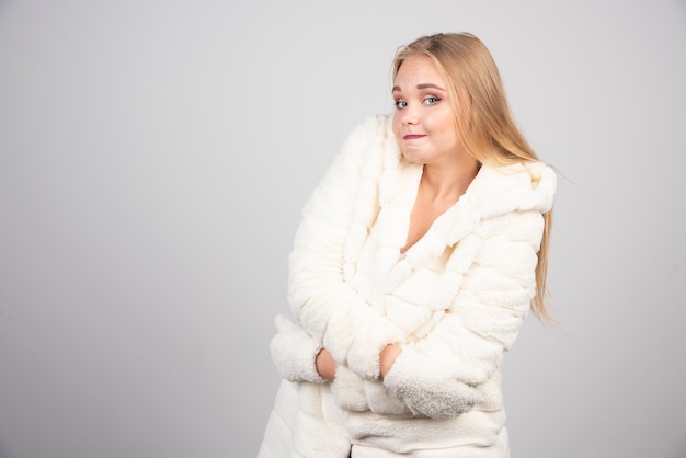 Schöne Frau im Winteroutfit posiert auf grauer Wand.