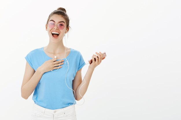 Schöne Frau in der Sonnenbrille, die Musik in den Kopfhörern unter Verwendung des Mobiltelefons hört