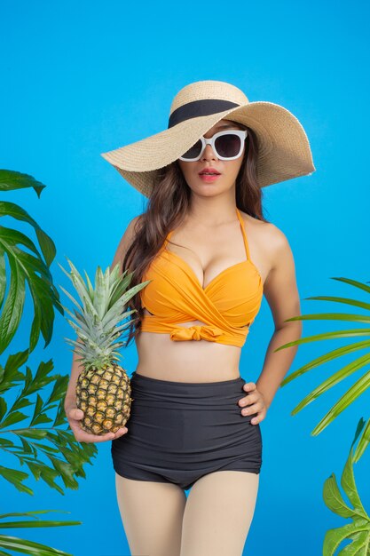 Schöne Frau in einem Badeanzug, der eine Ananas auf Blau anhält