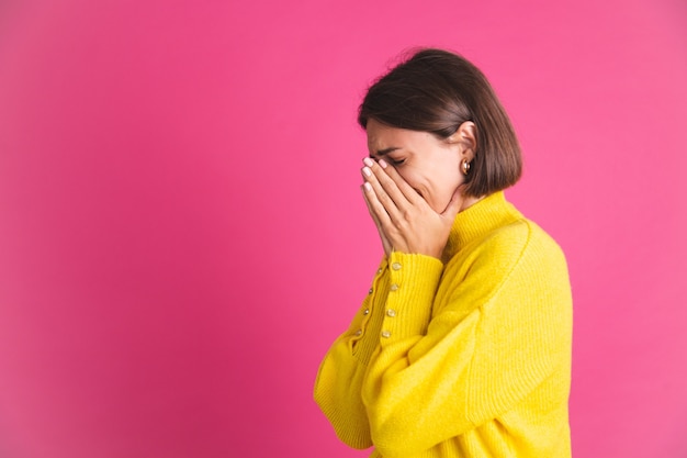 Schöne Frau in leuchtend gelbem Pullover isoliert auf rosa stressiger weinender Depression