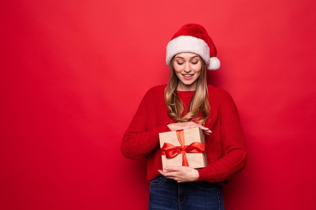 Schöne Frau in Weihnachtsmütze mit Geschenkbox in Händen isoliert auf roter Wand