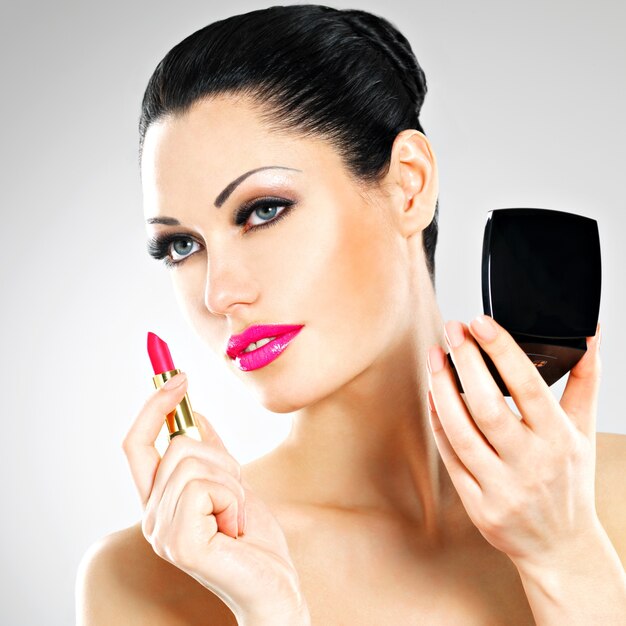 Schöne Frau macht Make-up, das rosa Lippenstift auf Lippen anwendet.