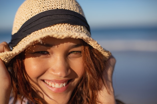 Schöne Frau mit dem Hut, der Kamera auf Strand im Sonnenschein betrachtet