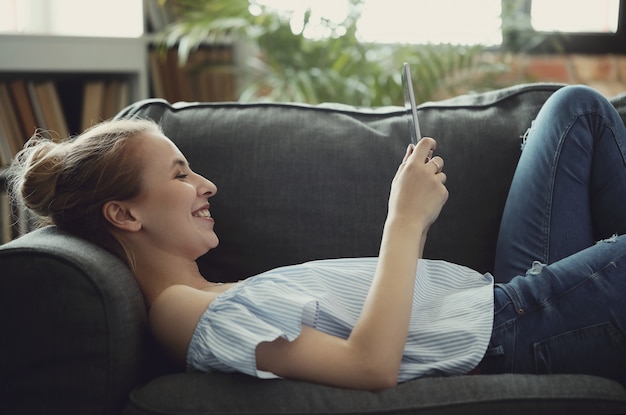 Schöne Frau mit digitaler Tablette, auf Sofa liegend