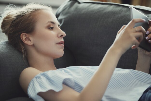 Schöne Frau mit digitaler Tablette, auf Sofa liegend