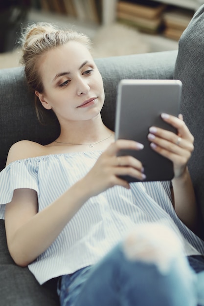 Kostenloses Foto schöne frau mit digitaler tablette, auf sofa liegend