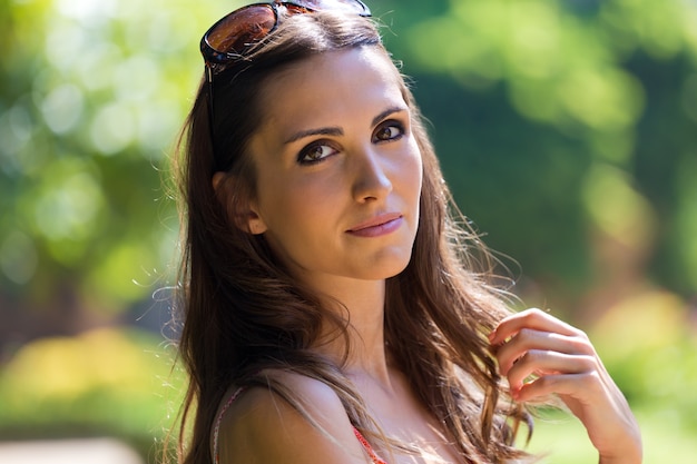 Schöne Frau mit dunklen Haaren und braunen Augen posiert im Sommergarten.