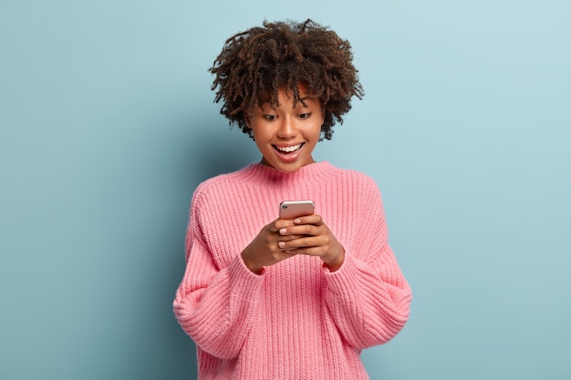 Schöne frau mit einem afro, der in einem rosa pullover aufwirft