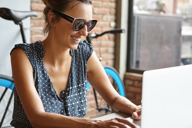 Schöne Frau mit glücklichem Lächeln, die Freunde online über soziale Medien unter Verwendung der drahtlosen Internetverbindung mitteilt