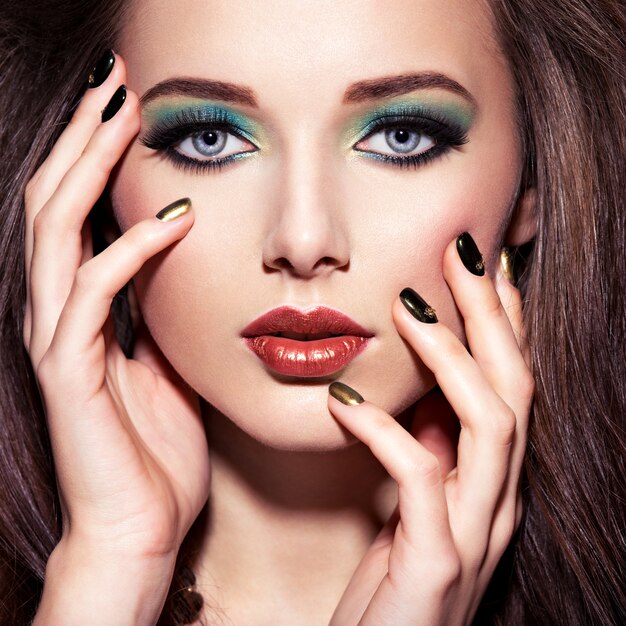 Schöne Frau mit grünem Make-up und kreativer Farbe der Nägel