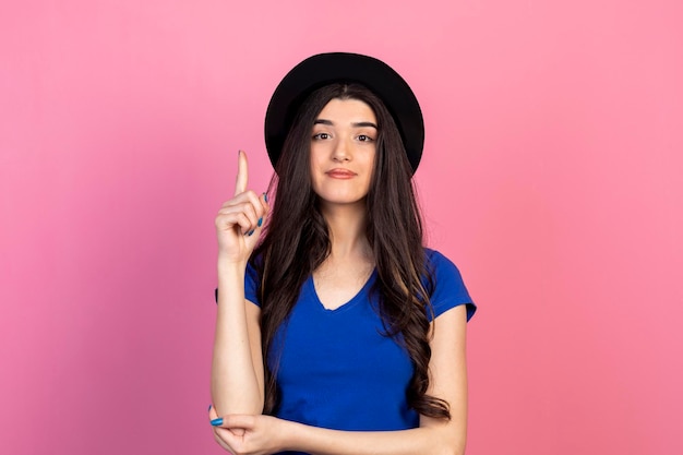 Schöne Frau mit Hut mit blauem T-Shirt und erhobenem Finger Foto in hoher Qualität