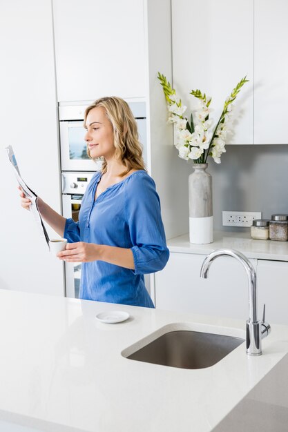 Schöne Frau mit Kaffeetasse und Zeitung lesen