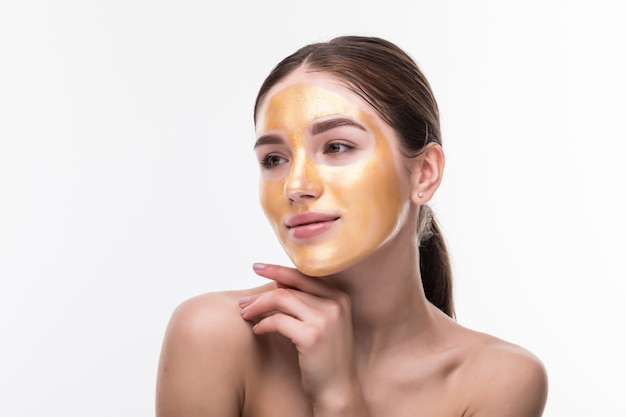 Schöne Frau mit kosmetischem Berührungsgesicht der goldenen Haut lokalisiert auf weißer Wand. Schönheitspflege und -behandlung